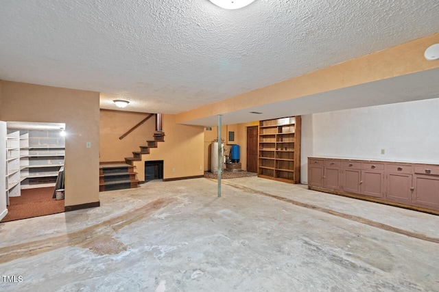 finished basement featuring stairway, baseboards, water heater, and a textured ceiling