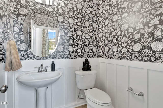 half bathroom with a wainscoted wall, toilet, and wallpapered walls