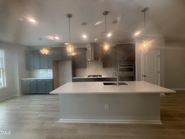 kitchen with baseboards, wall chimney range hood, light countertops, a sink, and appliances with stainless steel finishes