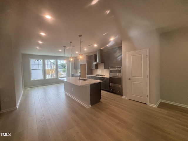 kitchen with baseboards, wall chimney range hood, a sink, light wood-style flooring, and appliances with stainless steel finishes