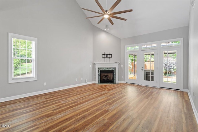 unfurnished living room with wood finished floors, baseboards, ceiling fan, high vaulted ceiling, and a premium fireplace