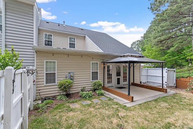 back of house with fence, roof with shingles, a gazebo, a lawn, and a patio