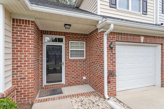 view of exterior entry featuring a garage and brick siding