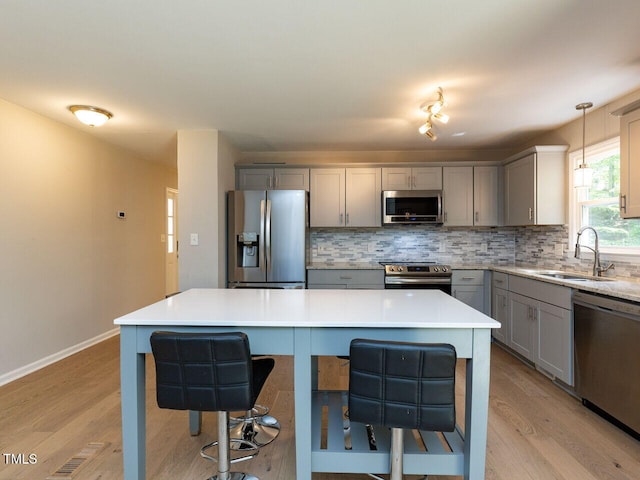 kitchen featuring a breakfast bar area, gray cabinetry, appliances with stainless steel finishes, and a sink