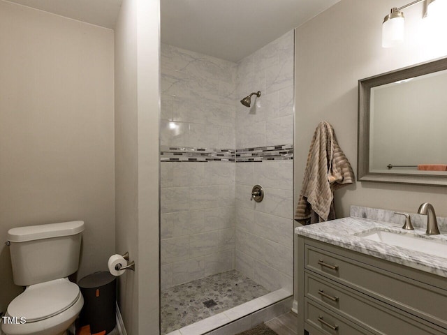 bathroom featuring vanity, a tile shower, and toilet