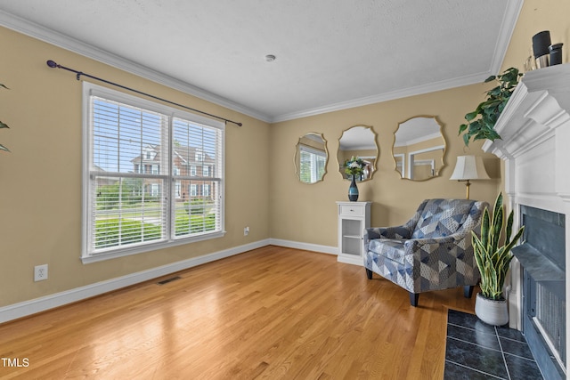 unfurnished room featuring visible vents, wood finished floors, a tile fireplace, baseboards, and ornamental molding