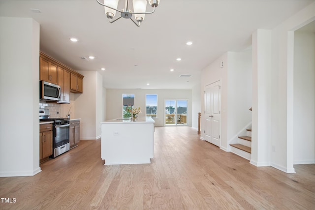 kitchen with stainless steel appliances, brown cabinets, light wood-style flooring, and a notable chandelier