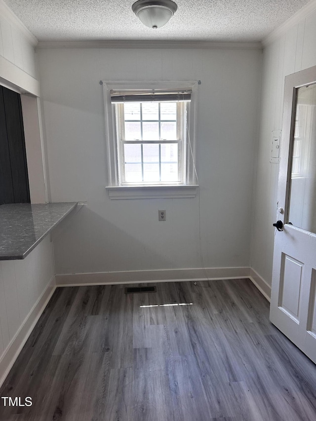 unfurnished dining area with visible vents, ornamental molding, a textured ceiling, and wood finished floors