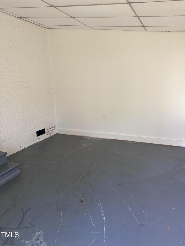 spare room featuring baseboards, a paneled ceiling, and concrete flooring