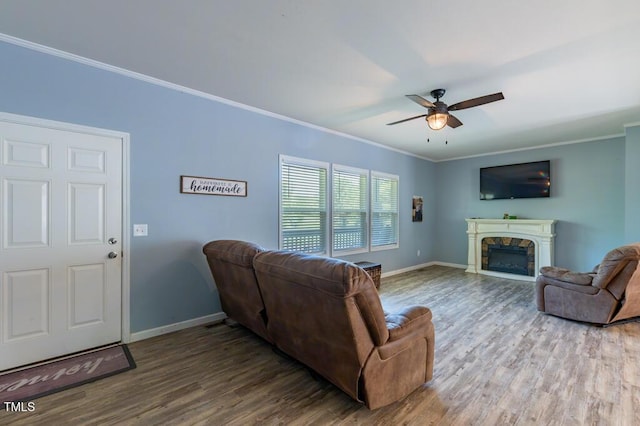 living area featuring ceiling fan, baseboards, wood finished floors, crown molding, and a fireplace