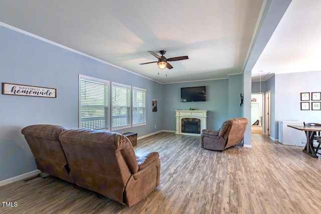 living area with a ceiling fan, wood finished floors, baseboards, and crown molding