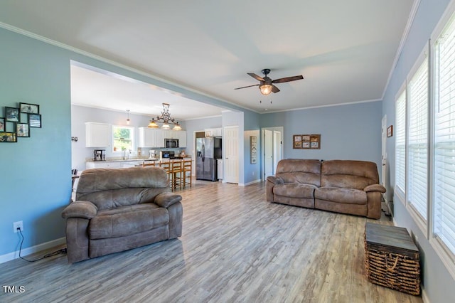 living area featuring a ceiling fan, light wood-style flooring, baseboards, and crown molding