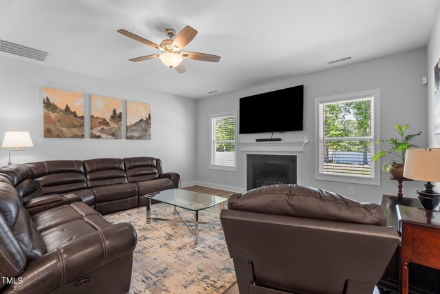living area with a ceiling fan, a fireplace, wood finished floors, and baseboards