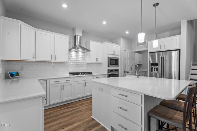kitchen with appliances with stainless steel finishes, a sink, wall chimney exhaust hood, a kitchen breakfast bar, and dark wood-type flooring