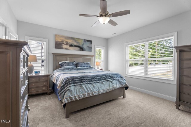 bedroom with light colored carpet, multiple windows, baseboards, and a ceiling fan