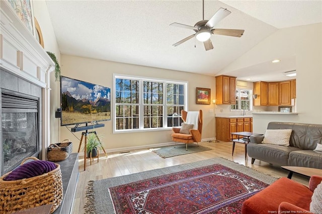 living room featuring a ceiling fan, baseboards, vaulted ceiling, and light wood finished floors