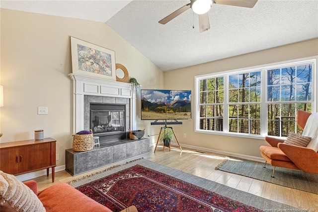 living area with wood finished floors, a fireplace, baseboards, a ceiling fan, and vaulted ceiling