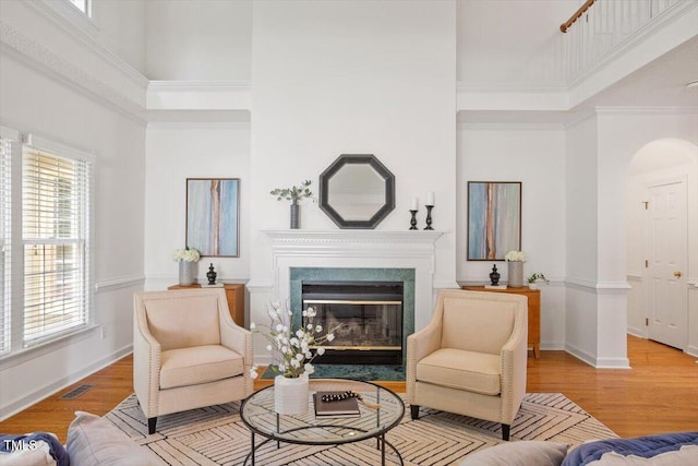 living room with a high ceiling, a fireplace with flush hearth, healthy amount of natural light, arched walkways, and wood finished floors