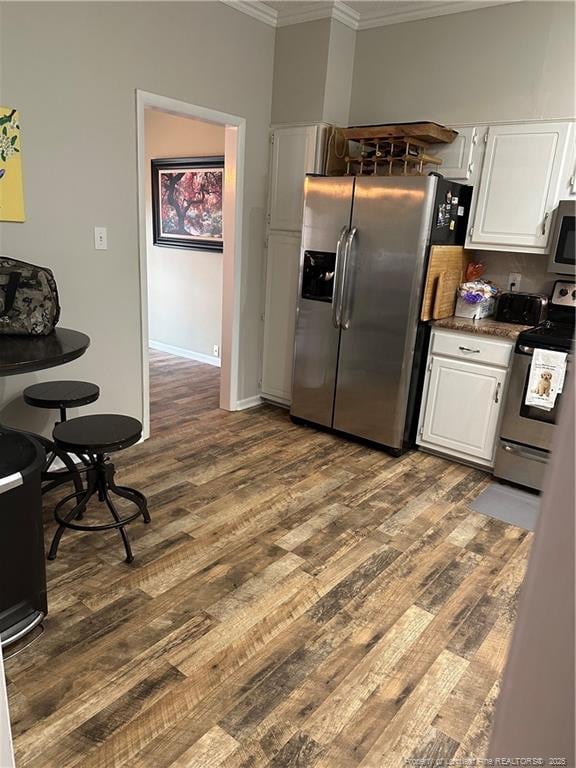 kitchen featuring dark wood-style flooring, dark countertops, ornamental molding, stainless steel appliances, and white cabinetry