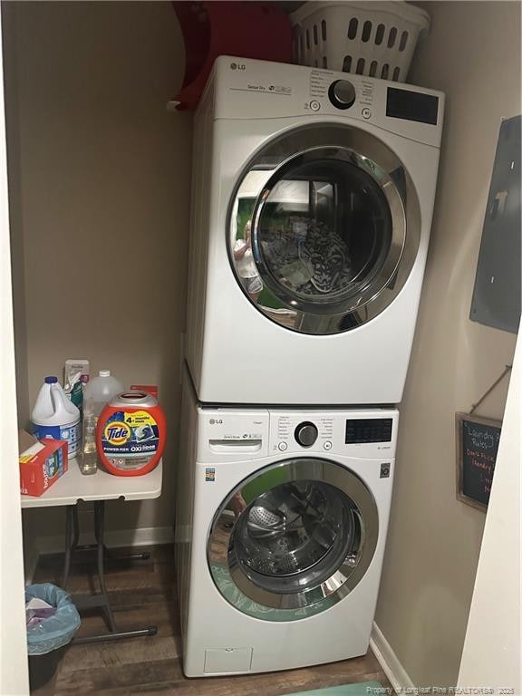 clothes washing area with baseboards, stacked washer and dryer, laundry area, and wood finished floors