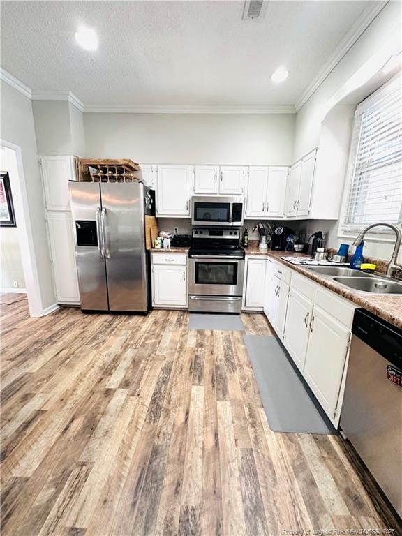 5706 Archer Rd, Hope Mills, NC 28348 - kitchen featuring appliances with stainless steel finishes, a sink, light wood-style floors, white cabinetry, and crown molding