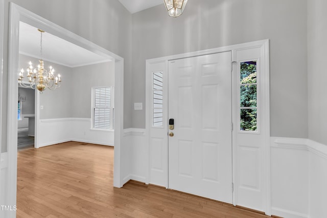 entryway featuring crown molding, an inviting chandelier, wainscoting, and light wood-type flooring
