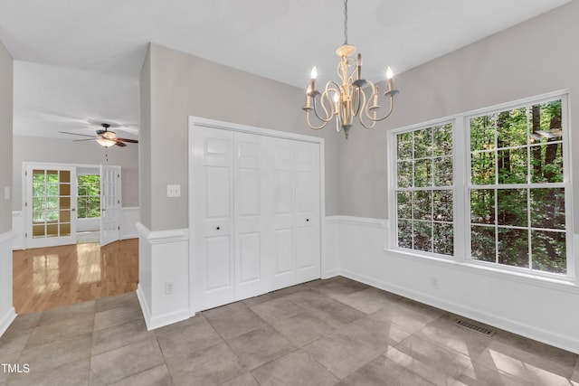 unfurnished dining area with light tile patterned floors, a wainscoted wall, ceiling fan with notable chandelier, and visible vents