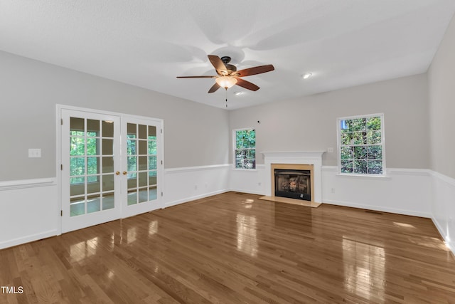 unfurnished living room featuring ceiling fan, french doors, visible vents, a fireplace with flush hearth, and wood finished floors