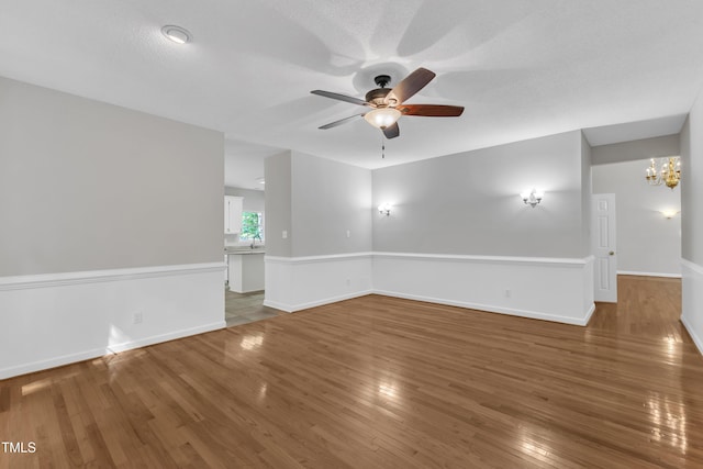 unfurnished room featuring wood-type flooring, baseboards, a sink, and ceiling fan with notable chandelier