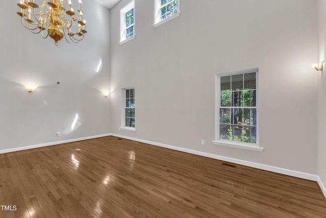 interior space featuring visible vents, wood finished floors, baseboards, an inviting chandelier, and a high ceiling