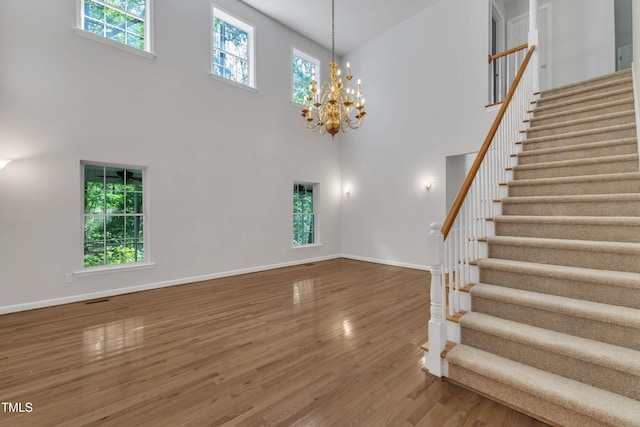 stairs featuring baseboards, a towering ceiling, wood finished floors, and an inviting chandelier