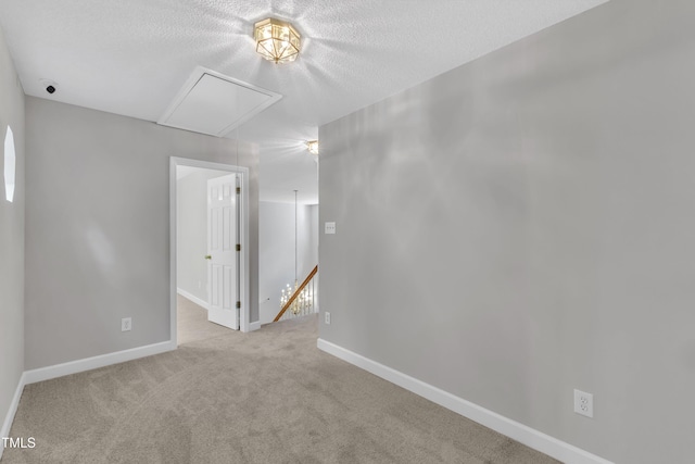 carpeted empty room featuring a textured ceiling, baseboards, and attic access