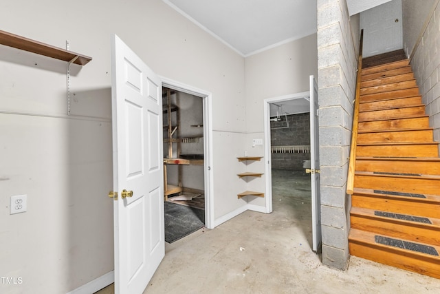 interior space with unfinished concrete flooring, ornamental molding, and stairway
