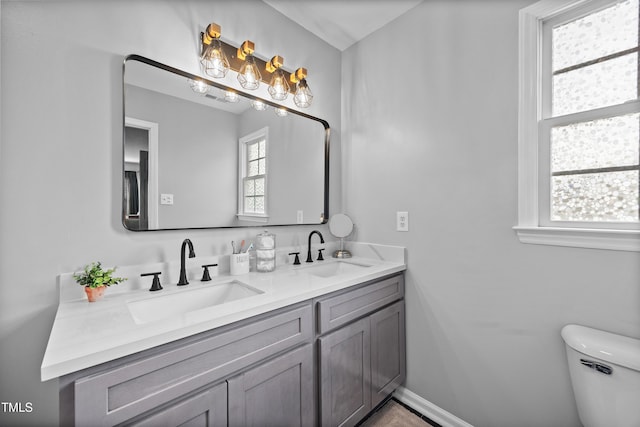 full bath featuring double vanity, toilet, baseboards, and a sink