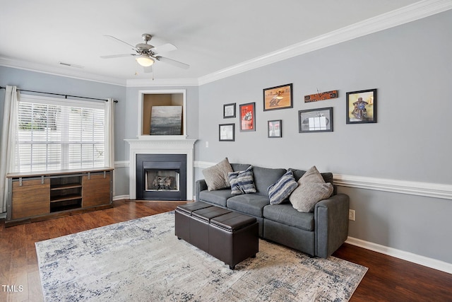 living room with wood finished floors, a fireplace, baseboards, ceiling fan, and ornamental molding