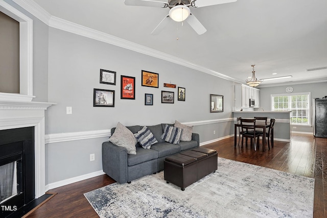 living area featuring crown molding, dark wood finished floors, a fireplace, and ceiling fan