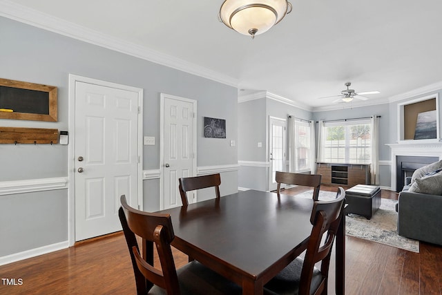 dining space featuring ceiling fan, a fireplace, ornamental molding, and dark wood-style floors