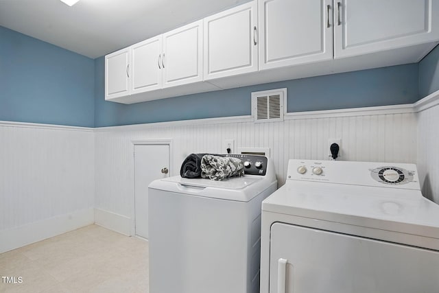 laundry area featuring separate washer and dryer, cabinet space, a wainscoted wall, and visible vents