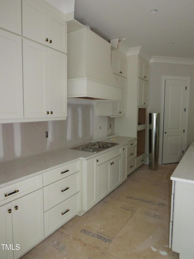 kitchen with crown molding, premium range hood, white cabinets, and stainless steel cooktop
