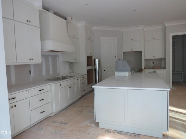 kitchen featuring wall chimney range hood, white cabinets, a kitchen island, and stovetop