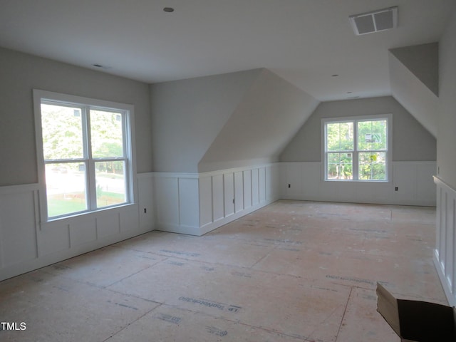additional living space featuring a decorative wall, wainscoting, lofted ceiling, and visible vents