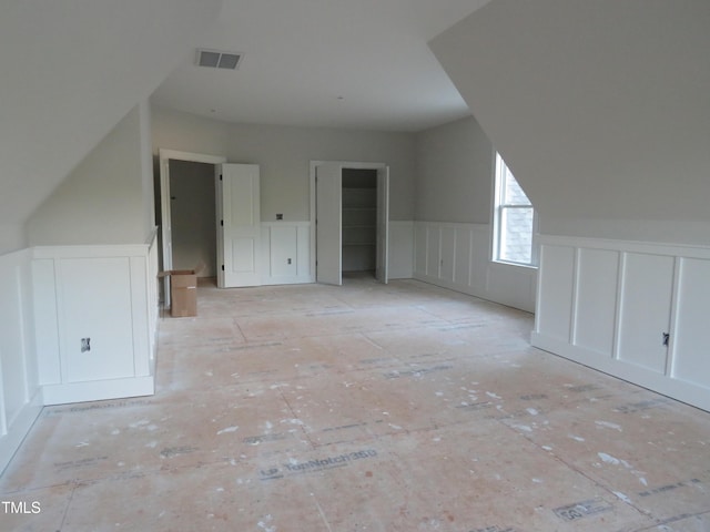 bonus room featuring visible vents, a wainscoted wall, lofted ceiling, and a decorative wall