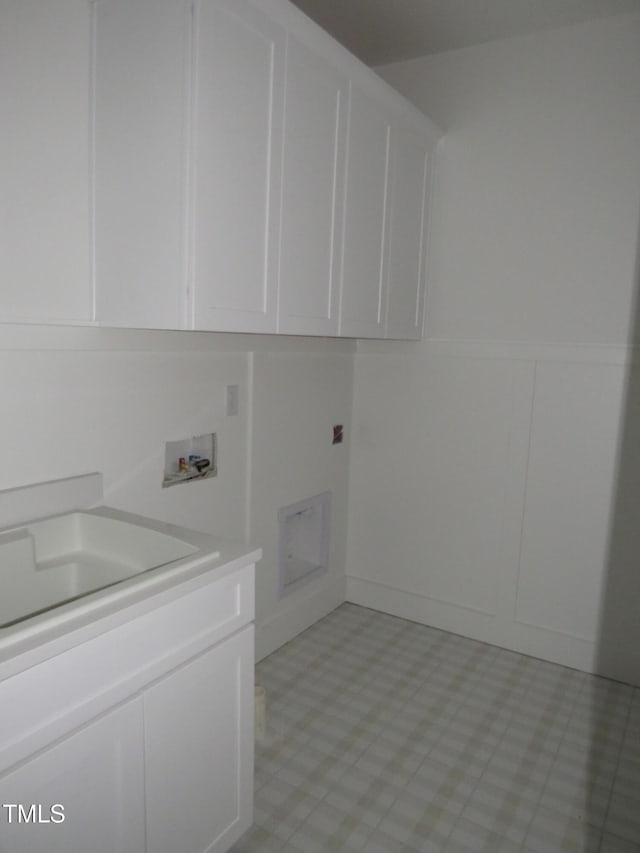 laundry area featuring a decorative wall, hookup for a washing machine, light floors, a sink, and cabinet space