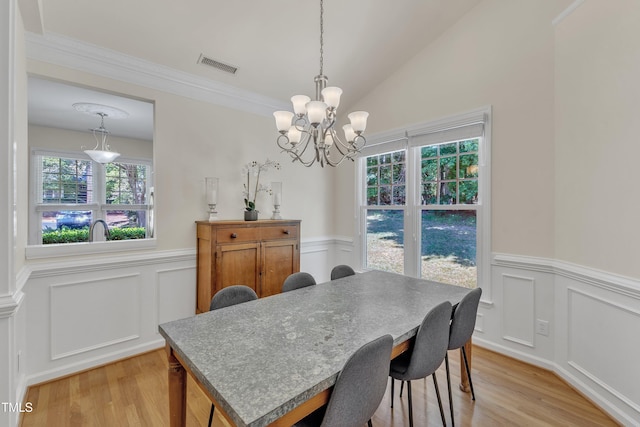 dining area featuring a wainscoted wall, a chandelier, light wood-style floors, a decorative wall, and lofted ceiling