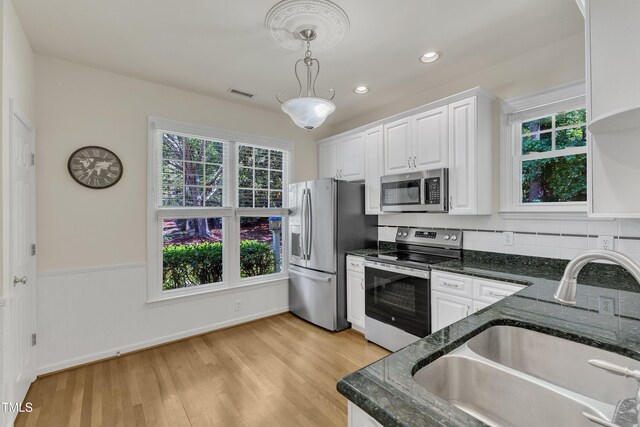 kitchen featuring appliances with stainless steel finishes, a sink, white cabinets, plenty of natural light, and a wainscoted wall