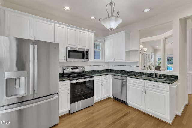 kitchen featuring appliances with stainless steel finishes, a sink, white cabinets, pendant lighting, and light wood finished floors