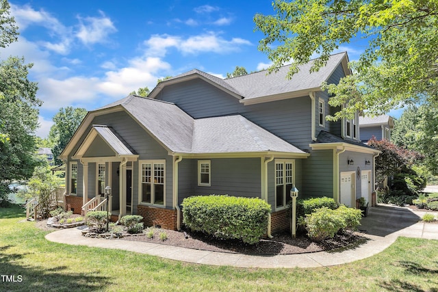 view of side of property with a shingled roof, a yard, driveway, and brick siding