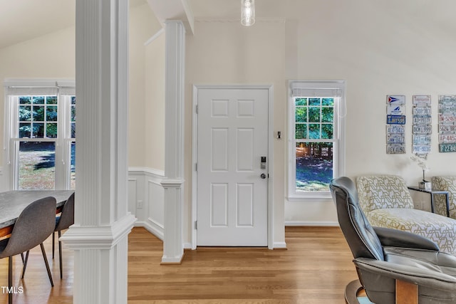 foyer with vaulted ceiling, light wood-style flooring, healthy amount of natural light, and ornate columns