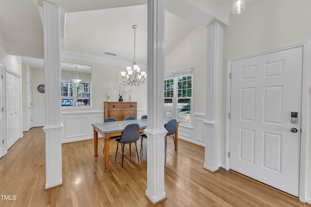 dining room with decorative columns, a decorative wall, a wainscoted wall, light wood-style floors, and a chandelier