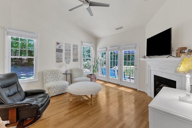 living area with light wood finished floors, a ceiling fan, a fireplace, and high vaulted ceiling